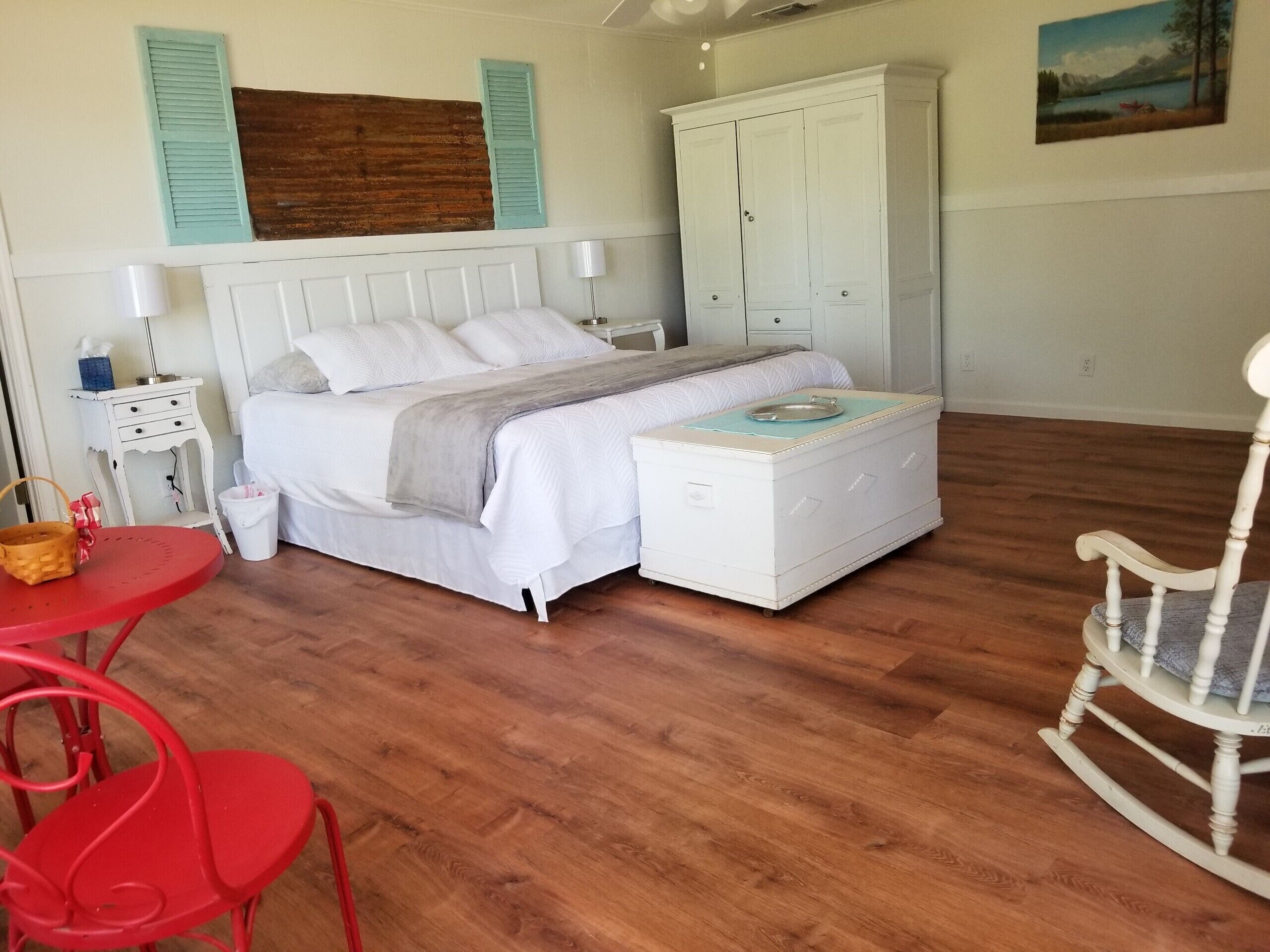 A bedroom with a bed, a dresser, a rocking chair, a table with chairs, and a painting on the wall.