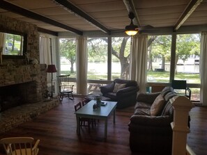 Ein gemütliches Wohnzimmer mit Kamin aus Stein, bequemen Sitzgelegenheiten und großen Fenstern mit Blick ins Freie.