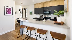 Une cuisine moderne avec des meubles en bois, un îlot central doté de tabourets et une grande fenêtre.