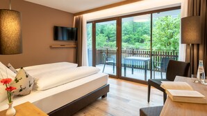 Una habitación de hotel con una cama grande, un televisor en la pared, una mesa de comedor con sillas y un balcón con vistas a zonas verdes.