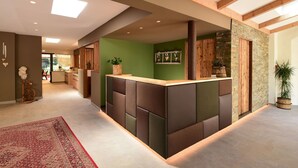 Una recepción moderna con un mostrador central, paredes verdes y techo de madera.