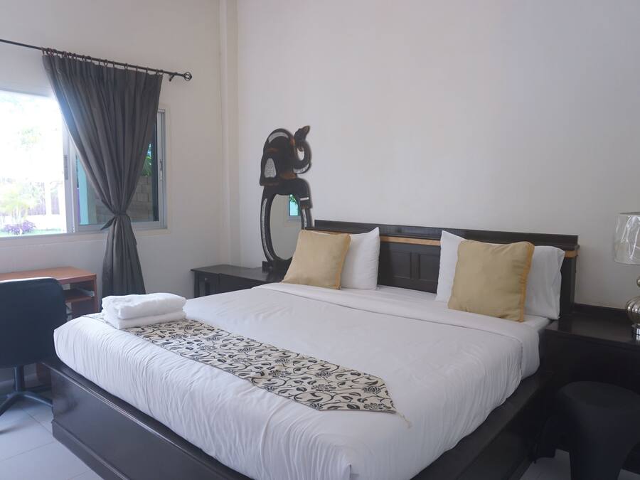 A hotel room with a large bed, a desk, a chair, a nightstand, a lamp, and a window with curtains.