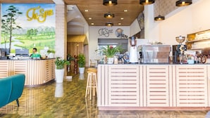 L'intérieur d'un café, avec un comptoir d'accueil en bois, un espace de travail pour les baristas et une fresque murale.