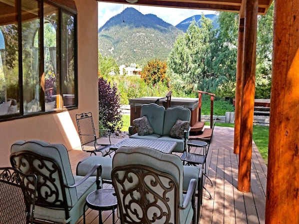 An outdoor patio with a sofa and chairs, a hot tub, and a view of mountains.
