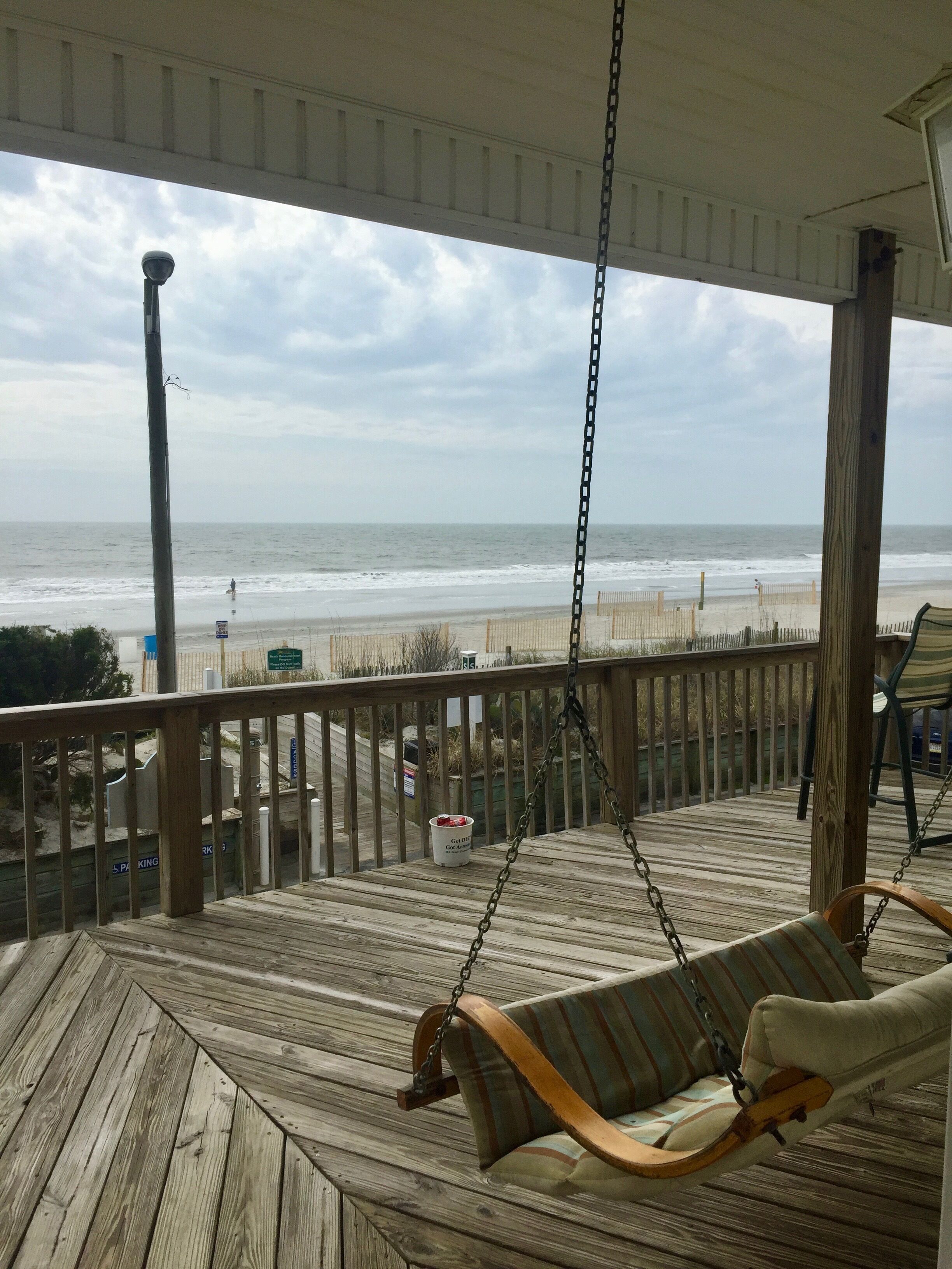 A wooden deck with a swing chair overlooking a beach.