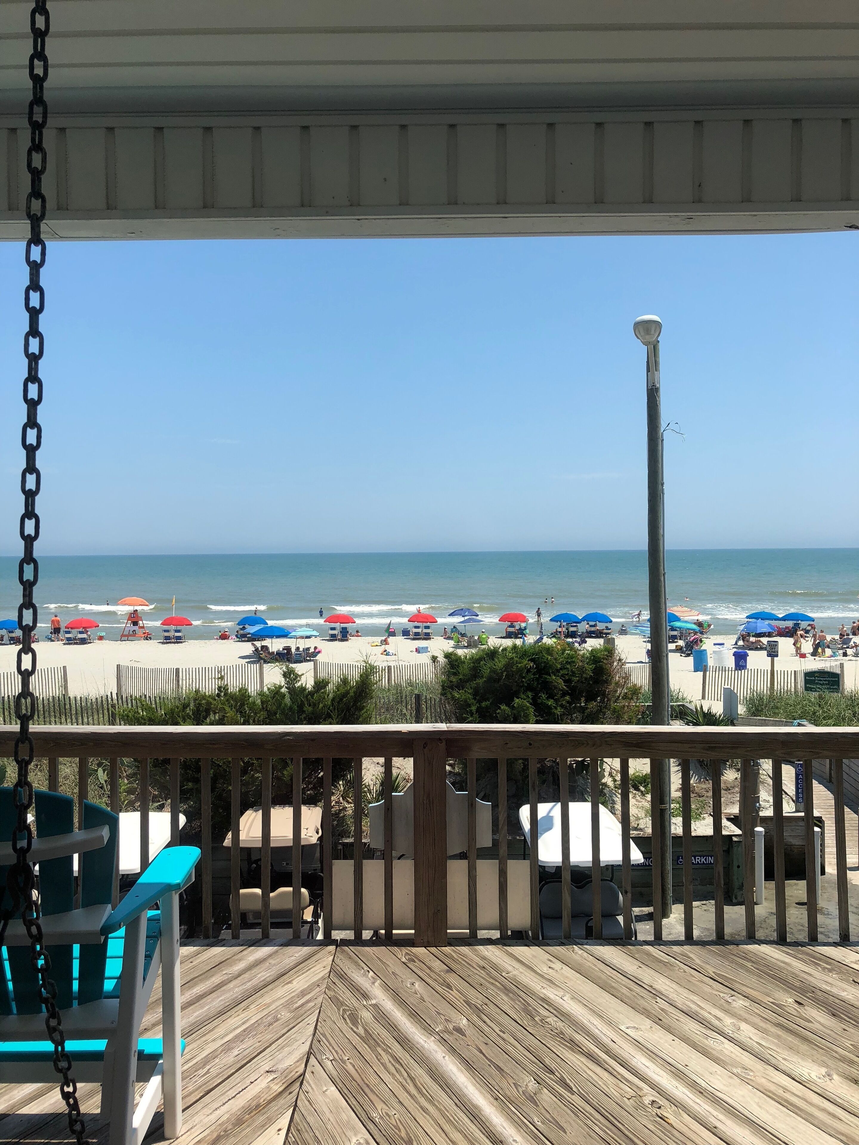 A wooden deck with a view of a beach with umbrellas and beach chairs.