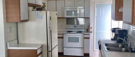 A compact kitchen with white cabinets, a built-in microwave, a stove, and a refrigerator.