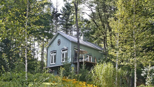 A house with a large deck, surrounded by dense trees and a pond.