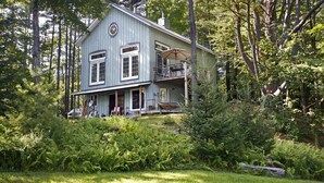 A two-story house with a balcony, surrounded by dense forest.