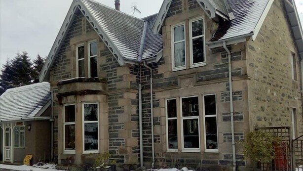 Een stenen huis met een steil dak, meerdere schoorstenen en een met sneeuw bedekte grond.