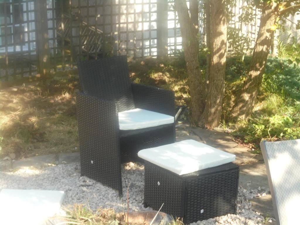 Buitenen meubels van riet met kussens, geplaatst op een grindpad, omgeven door bomen en een houten hek.