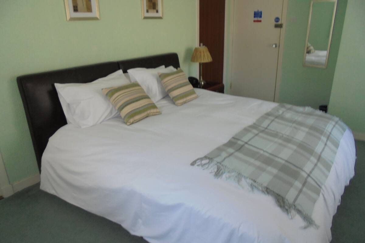 A neatly made bed with white linens and striped pillows, a plaid blanket, and a wooden headboard.
