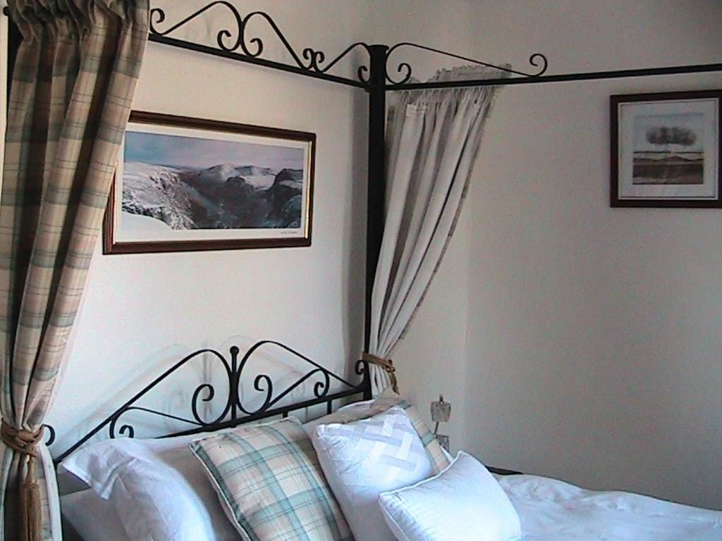 A four-poster bed with a metal frame, white bedding, and plaid pillows. There are two framed pictures on the wall, one above the bed and one to the right.