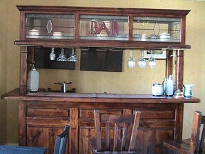 A bar area with a wooden counter, a glass display case, and hanging glassware. - Avondale House (Kingussie)