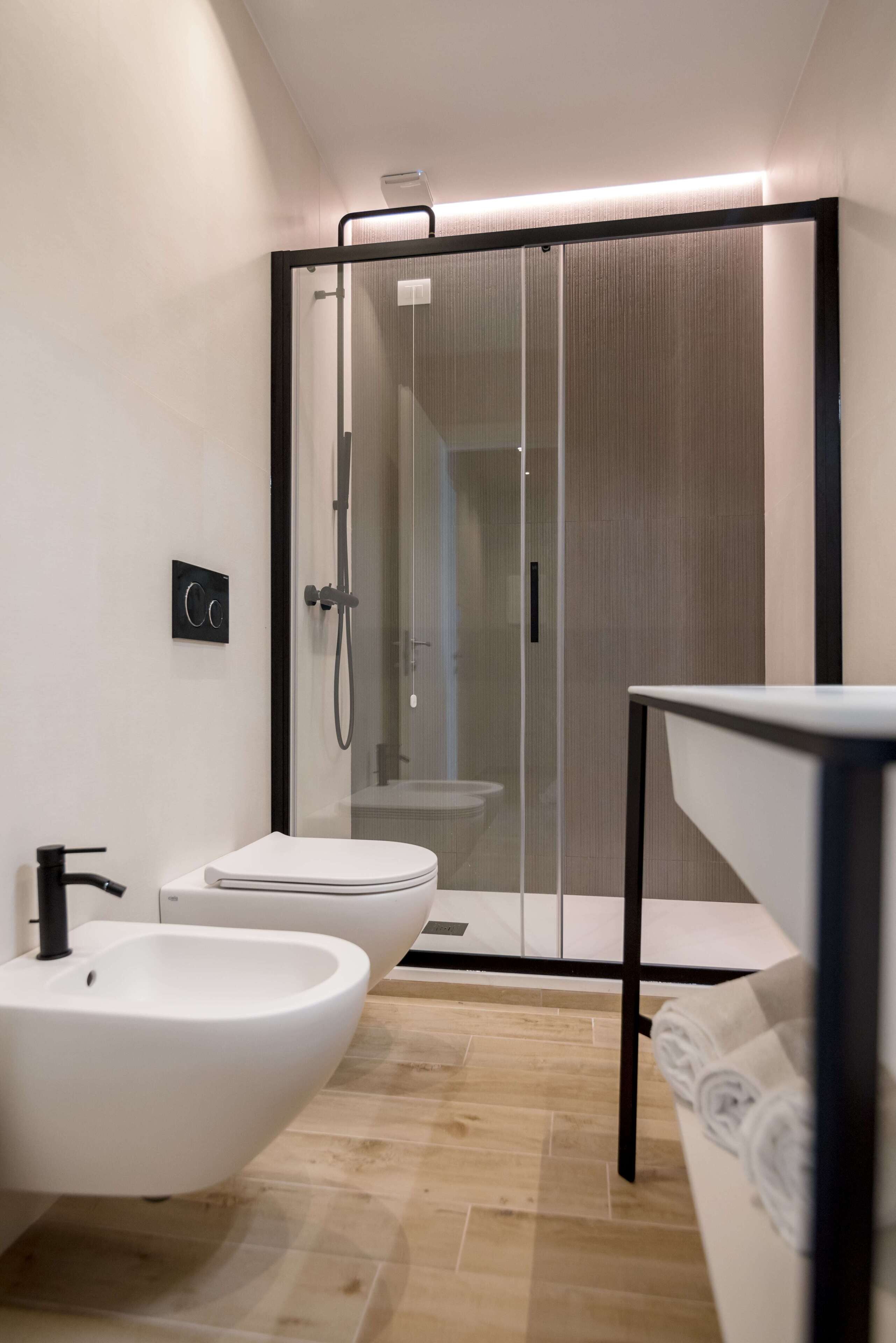 A modern bathroom with a glass-enclosed shower, a white sink, and a bidet.