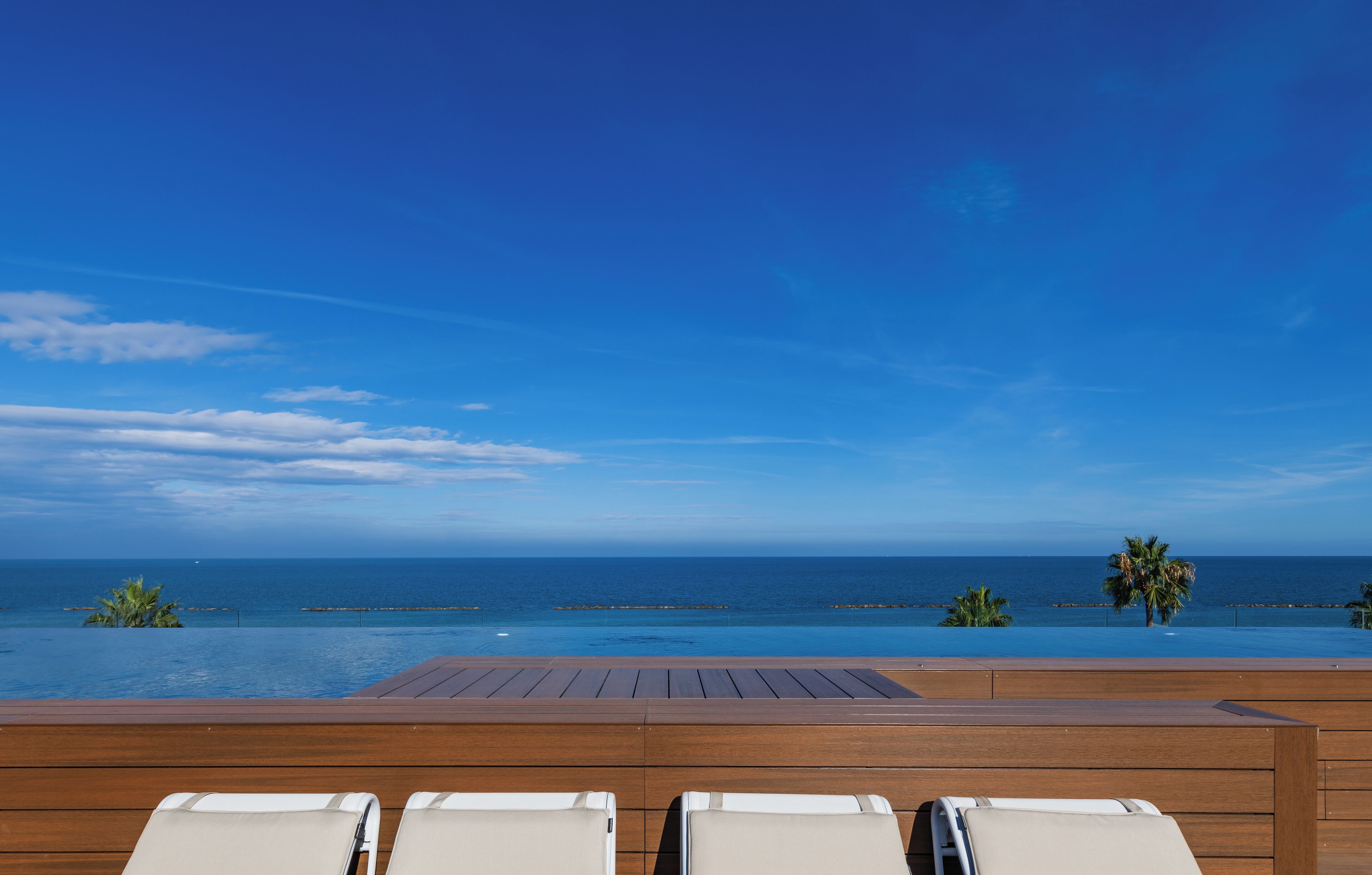 A wooden deck with lounge chairs overlooking a pool and ocean view.