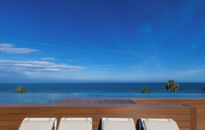 A wooden deck with lounge chairs overlooking a pool and ocean view.