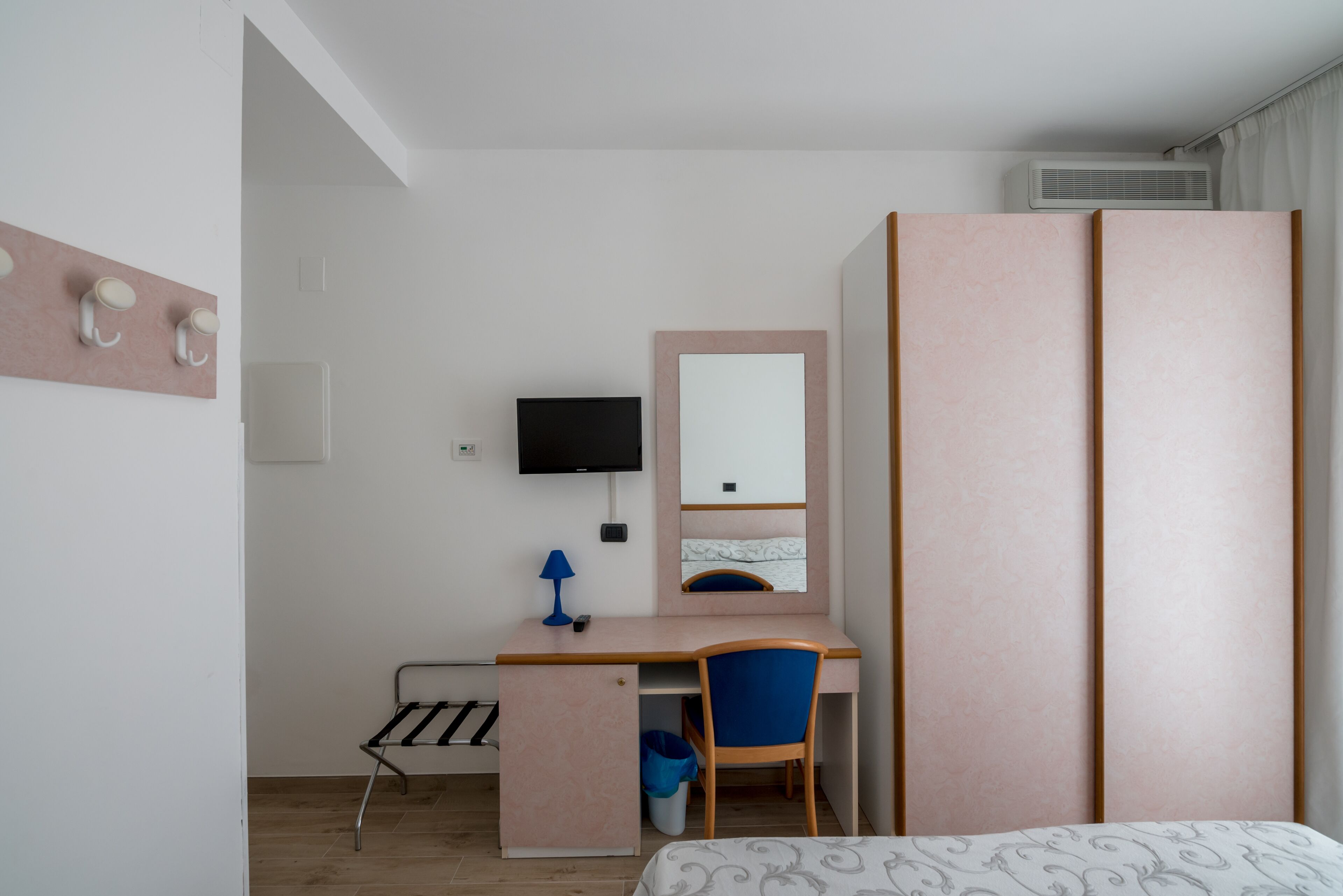 Un dormitorio con cama, escritorio, silla, televisor, armario y una ventana pequeña.