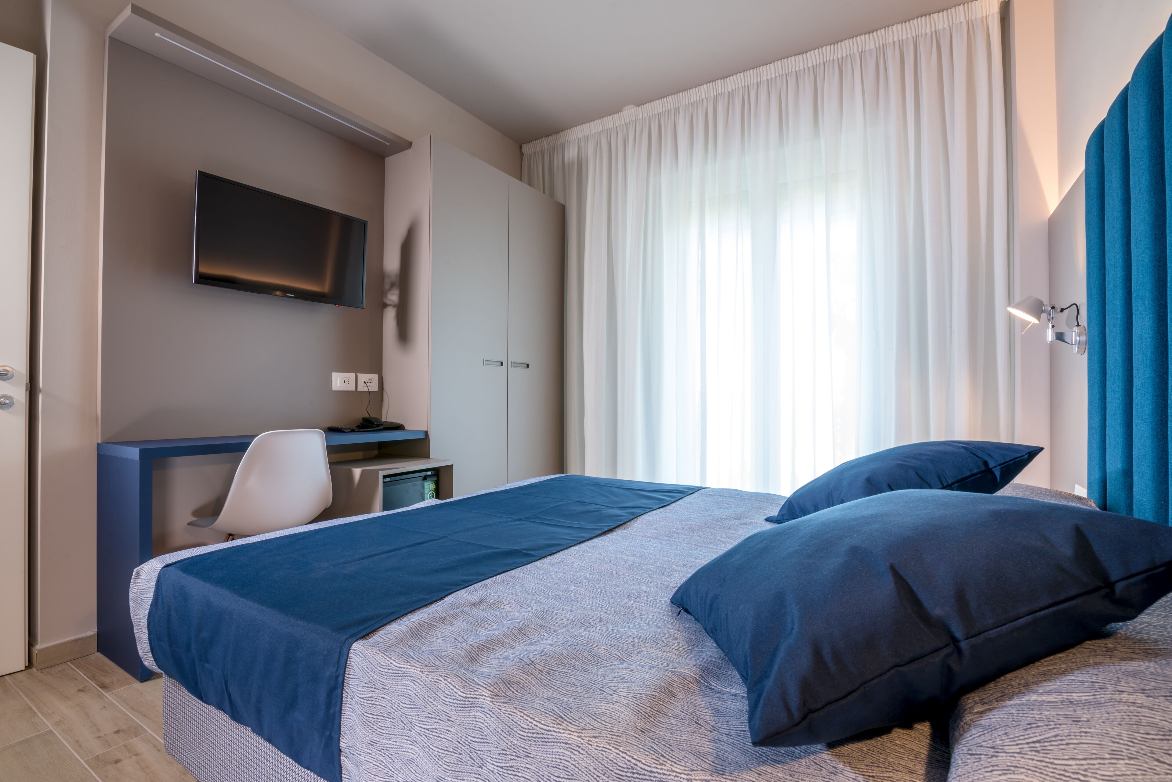 A modern hotel room with a bed, a desk, and a TV.