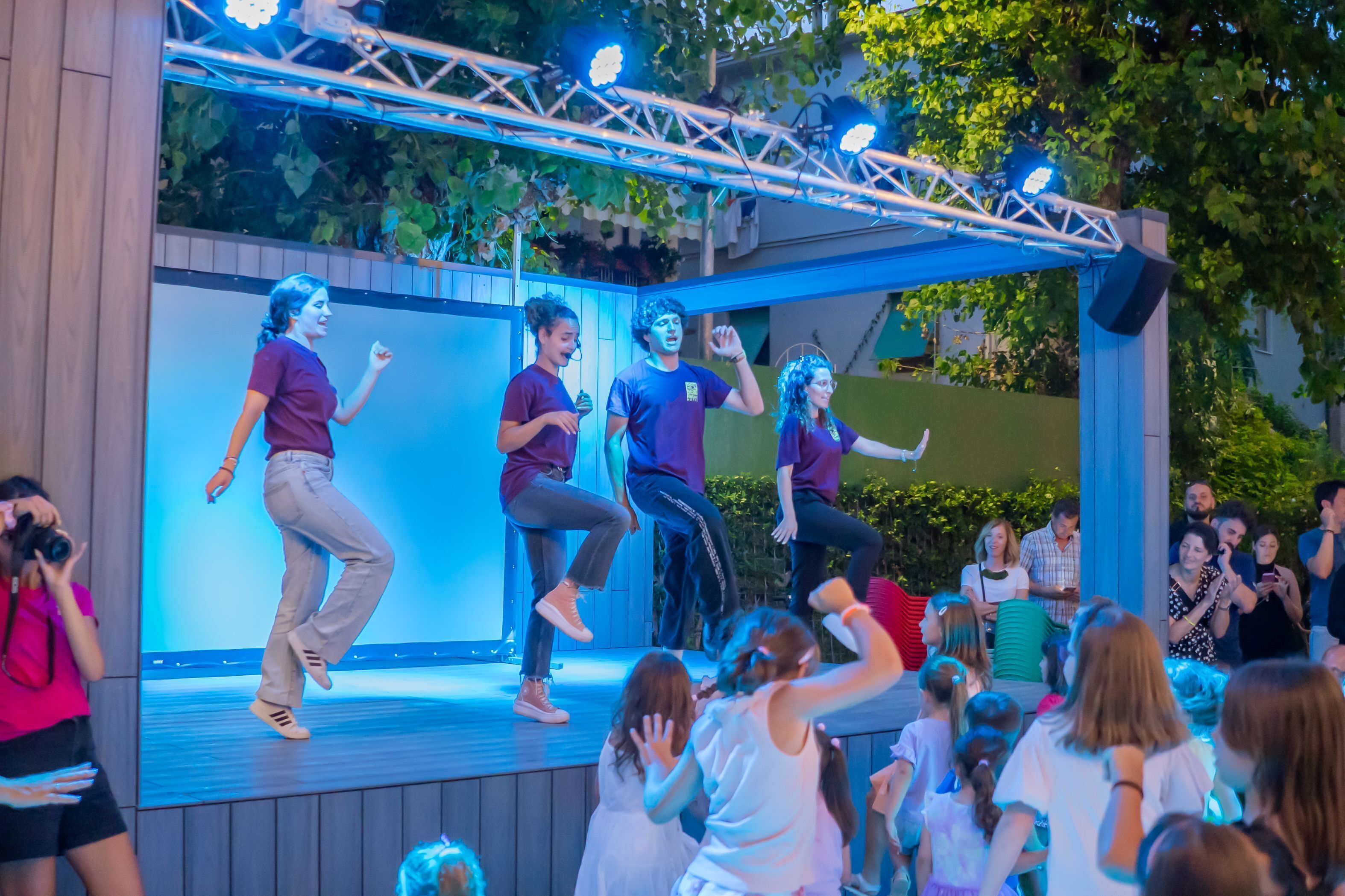 A stage with performers in casual attire, a crowd of spectators, and a backdrop with a geometric pattern.