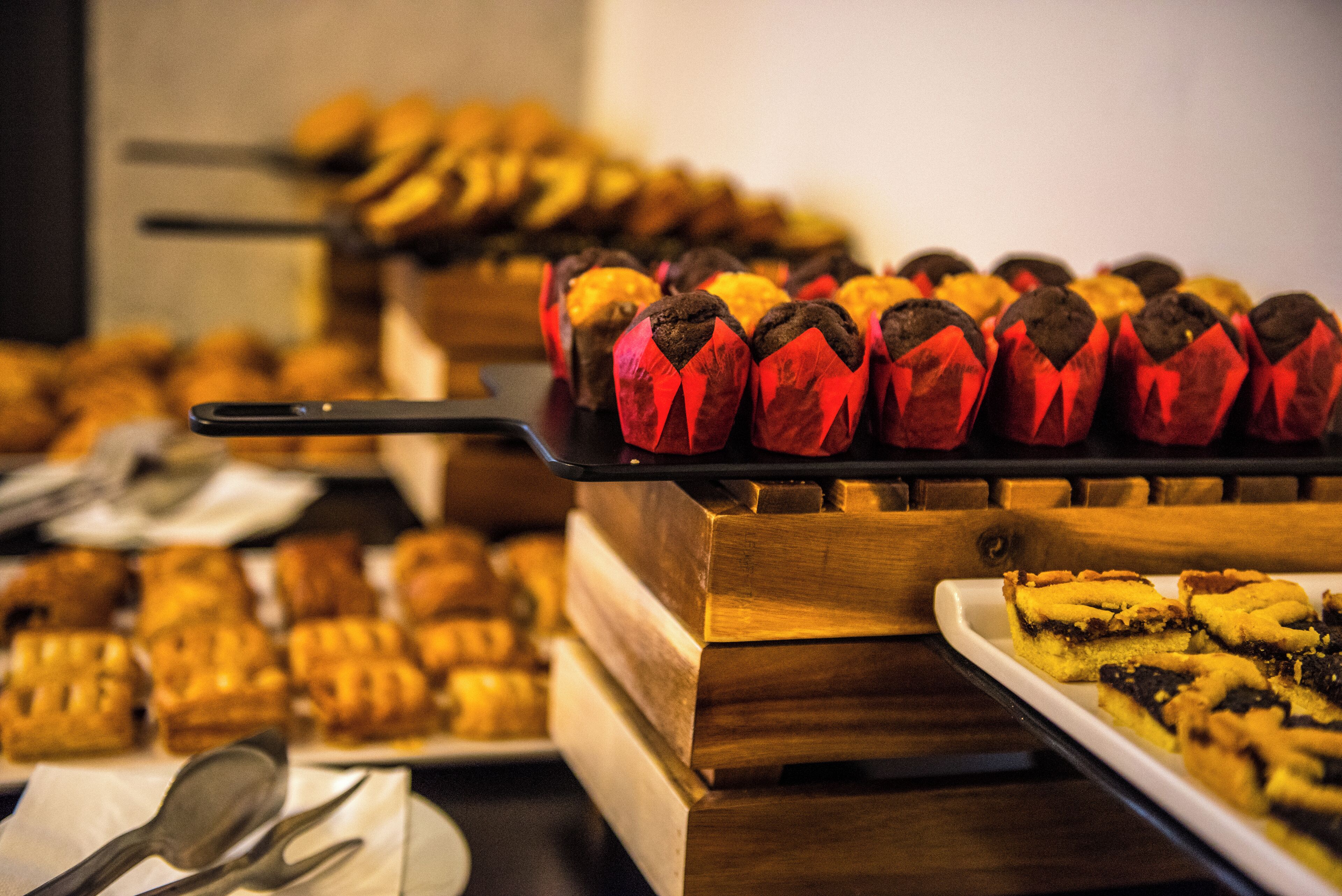 Un buffet proposant une variété de produits de boulangerie, notamment des muffins et des viennoiseries, présentés sur des présentoirs en bois.