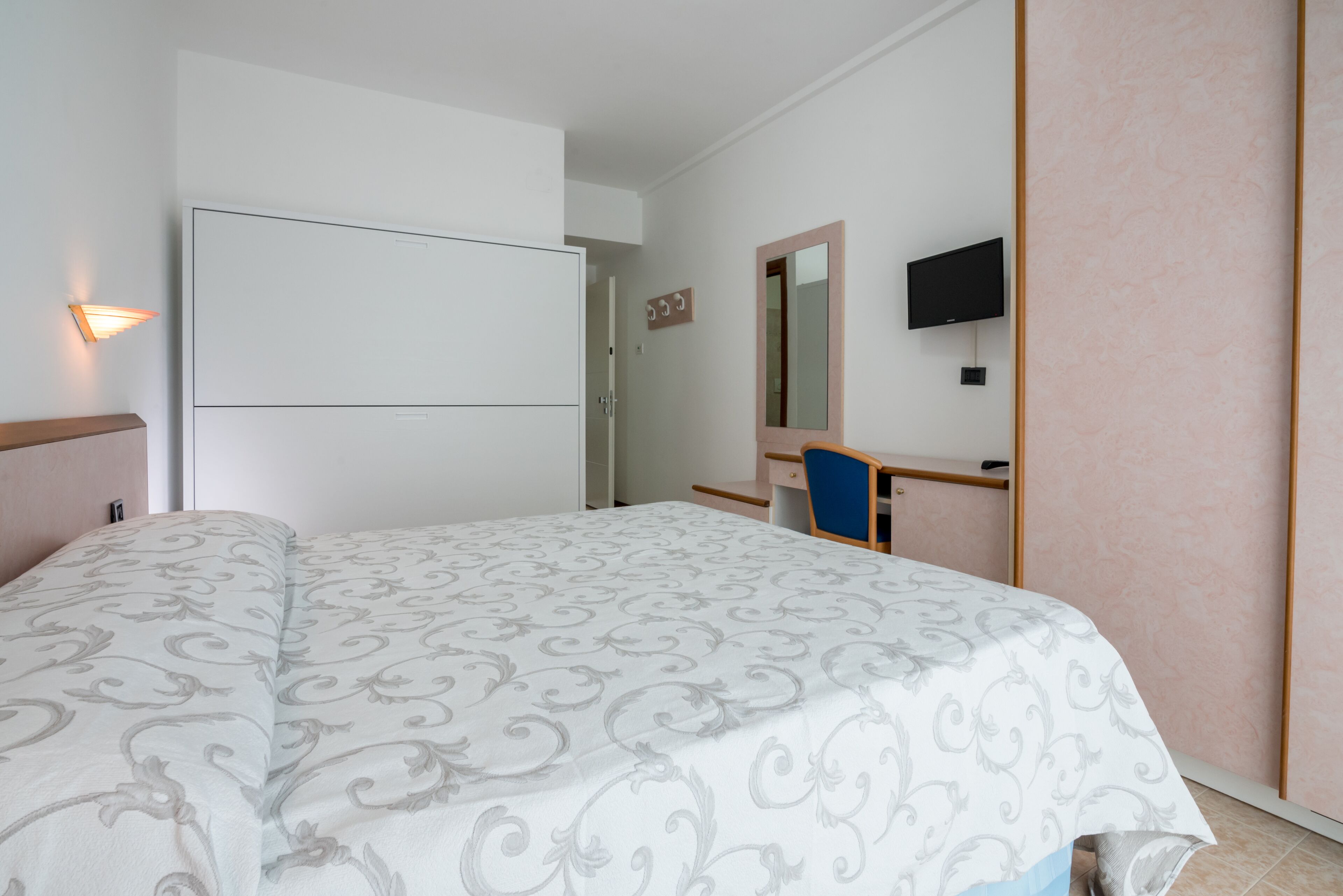 Una camera d'albergo con un letto, una scrivania, una sedia, una televisione e uno specchio.