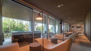 Uma área de estar moderna com paredes de vidro, assentos de couro e vista para o verde lá fora.