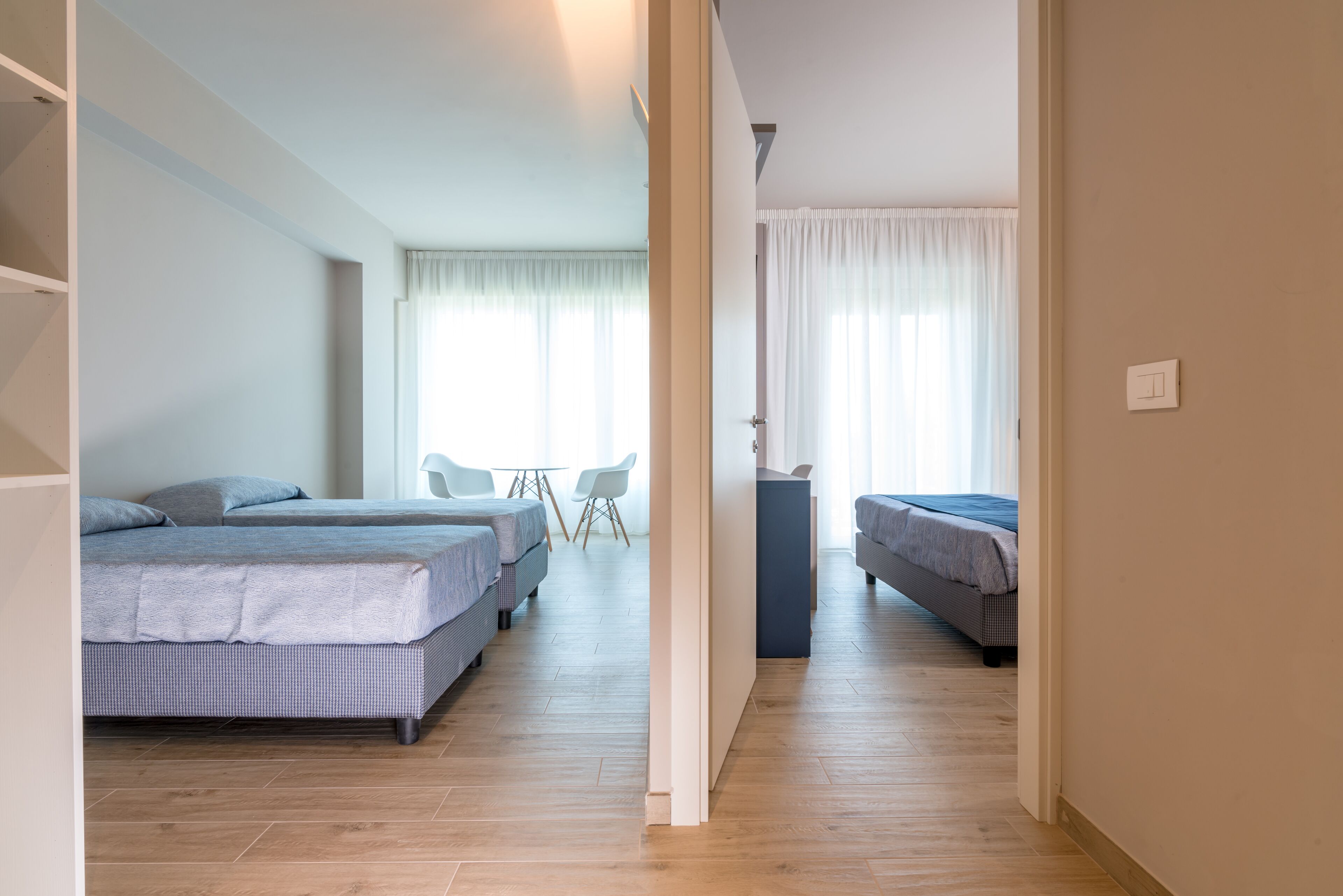 Quarto de hotel moderno com duas camas, uma mesinha e uma cadeira.