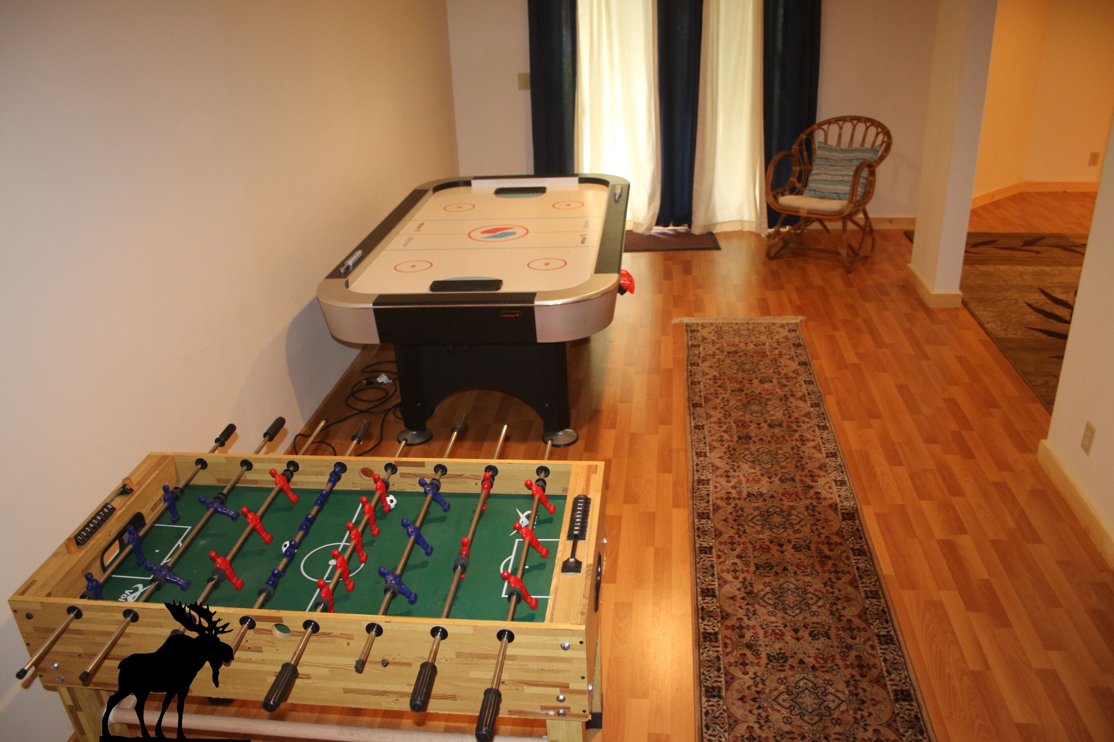 Une pièce avec deux tables de baby-foot, un plancher en bois et un tapis à motifs.
