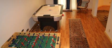 Une pièce avec deux tables de baby-foot, un plancher en bois et un tapis à motifs.