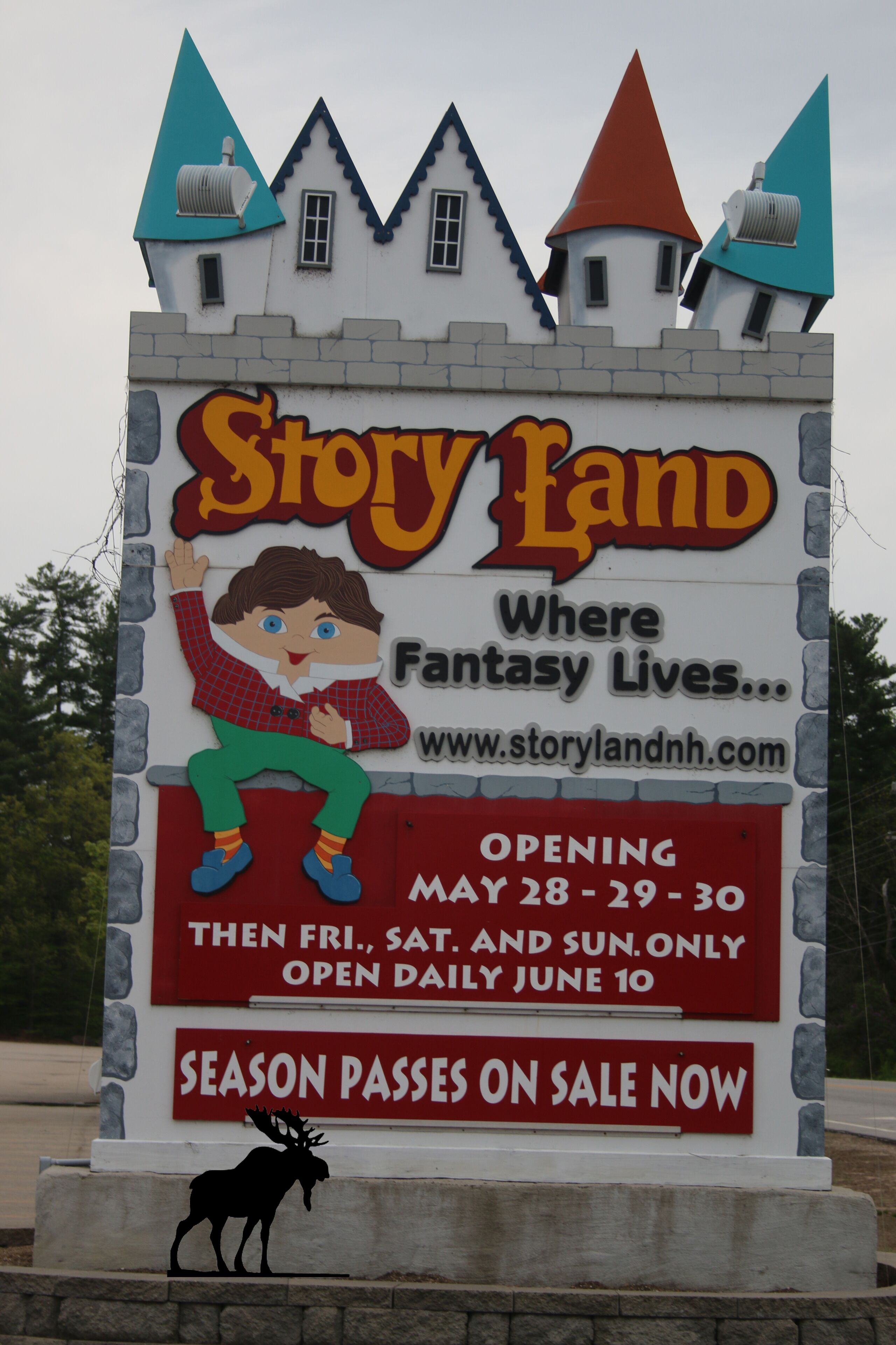 Skilt for Story Land med et slotlignende design, der viser en tegneseriefigur og tekst med åbningsdatoer samt tilbud på sæsonpas.