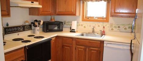 A kitchen with wooden cabinets, a stove, a microwave, a sink, and a dishwasher.