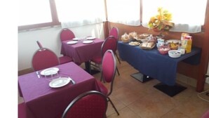 Uma área de refeições com mesas postas, cadeiras e um buffet com alimentos.