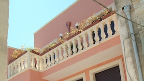 Um edifício de dois andares com fachada rosa, varanda com balaústres brancos e portão preto.