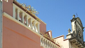 Um edifício com fachada rosa, portão preto, varanda branca e torre do relógio.