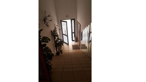 Um corredor com piso ladrilhado que leva a uma porta com vista para o exterior.