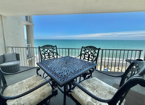 Ein Balkon mit einem Metalltisch und -stühlen mit Blick auf einen Strand.