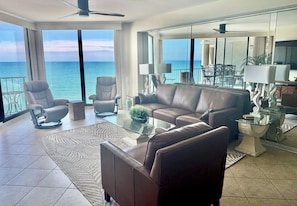 Una sala de estar moderna con una mesa de centro de vidrio, sofá de cuero y sillones, con vista a un balcón y al mar.