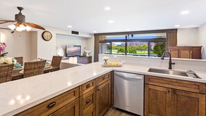 Una cocina moderna con una isla grande, armarios de madera, lavavajillas y vistas a un paisaje urbano a través de un ventanal.