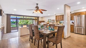 Cocina moderna con comedor, que incluye una isla grande, sillas de mimbre y un refrigerador de acero inoxidable.
