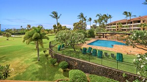 Zona de piscina con pared de piedra, sillas verdes y vistas a un campo de golf.