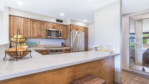 Cocina moderna con armarios de madera, electrodomésticos de acero inoxidable, encimera de mármol y una isla grande con taburetes.