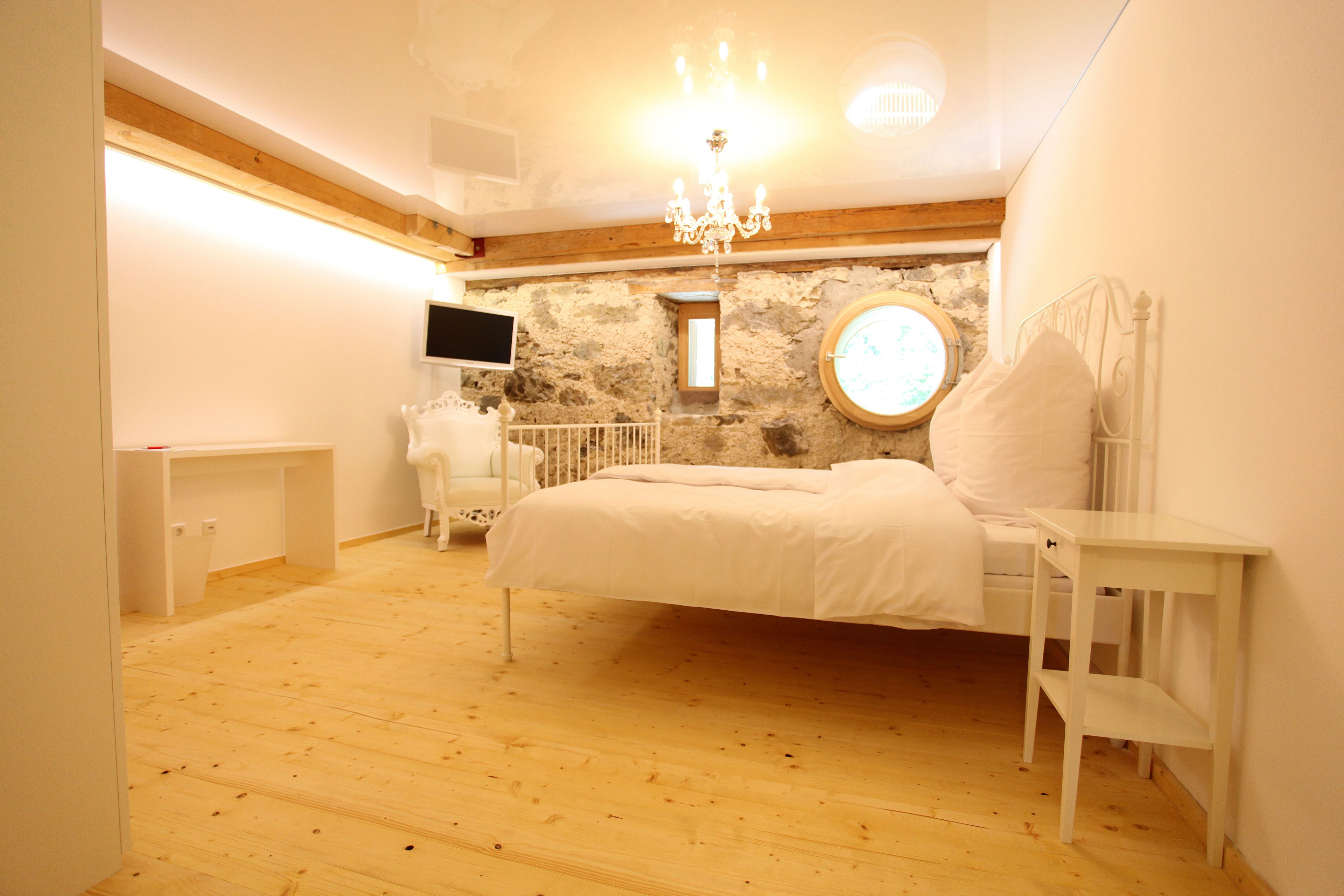 Una camera da letto con un letto, un comodino, una TV a parete e una parete in pietra.