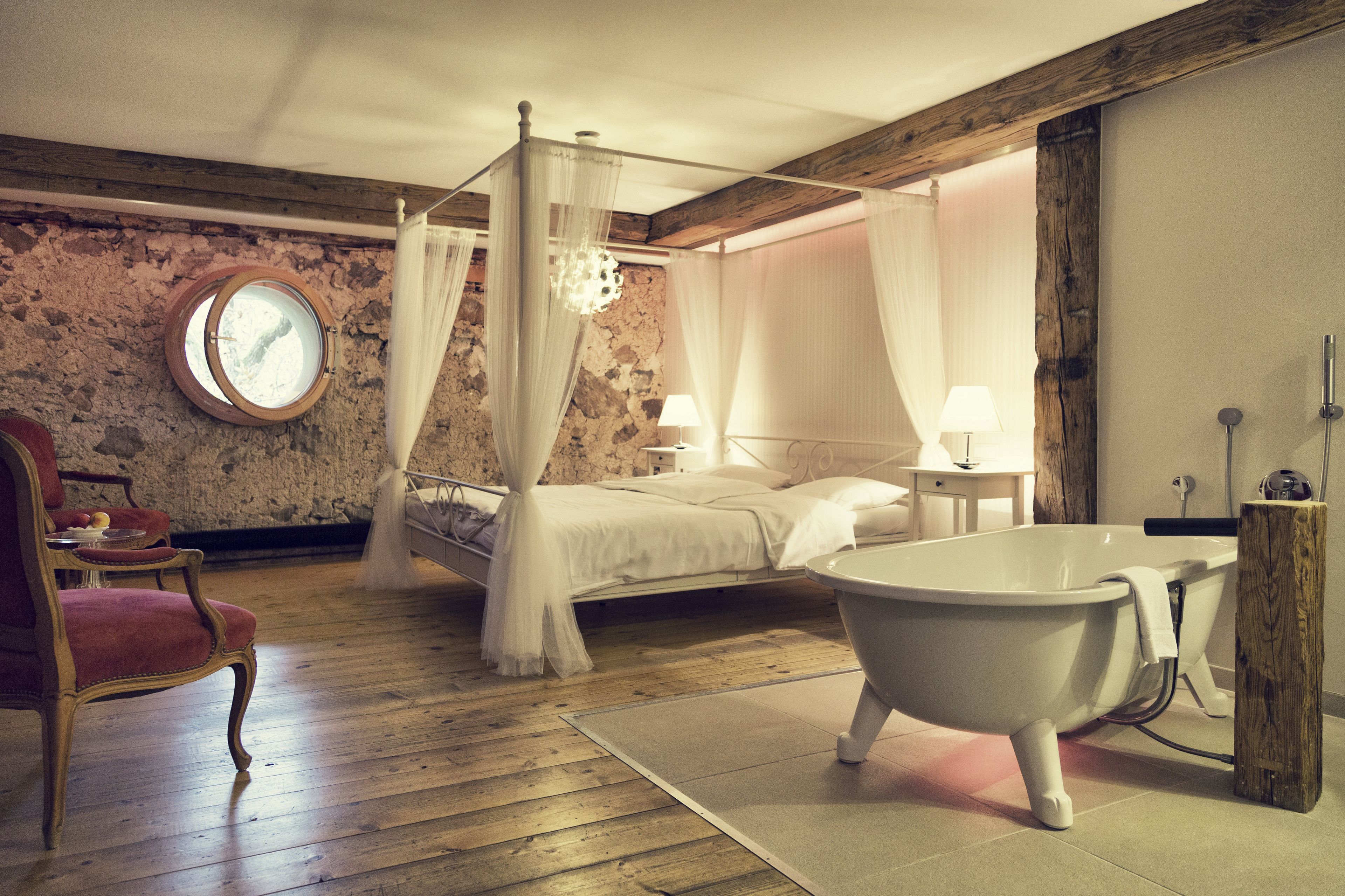 A bedroom with a four-poster bed, a clawfoot bathtub, and a stone wall.