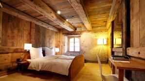 Una habitación de madera con cama, mesita de noche, lámpara y un escritorio con silla.