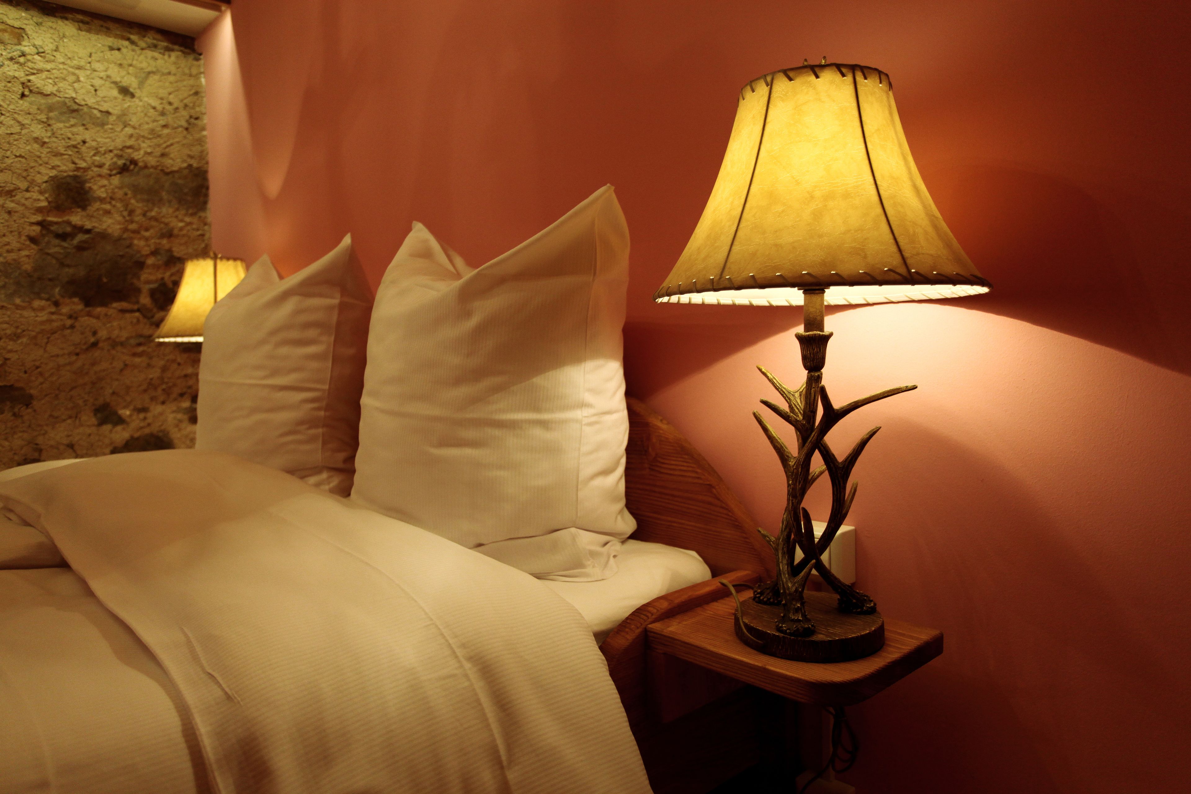 A bed with white bedding and pillows, a lamp with a decorative base, and a textured wall in the background.