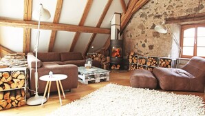 Una sala de estar acogedora con pared de piedra, vigas de madera, chimenea y sofá.