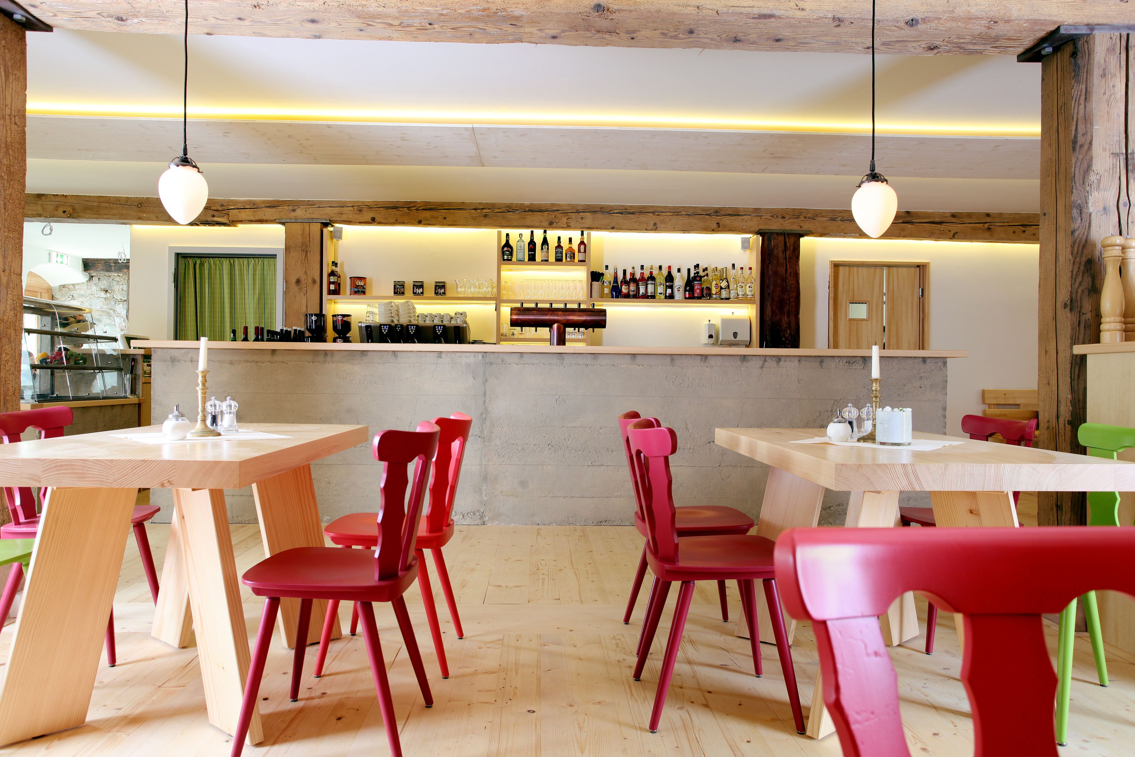 Un restaurante con mesas de madera y sillas rojas, una zona de bar con botellas y un ambiente rústico.