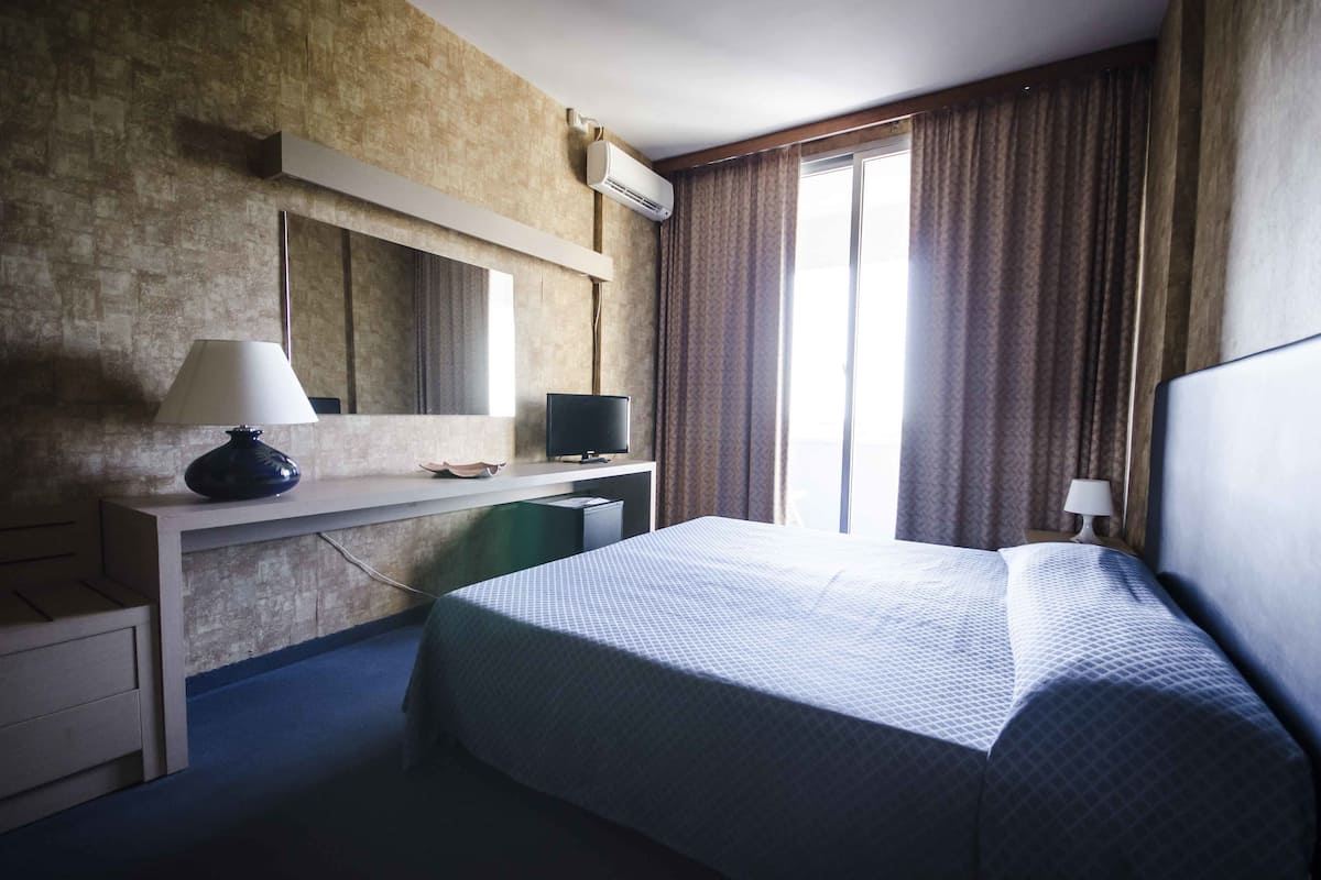 Une chambre d’hôtel avec un lit, un bureau et une grande fenêtre avec des rideaux.