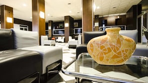 A hotel lobby with leather seating, a large decorative vase, and a checkered floor. - Hotel Helios (Tarquinia)